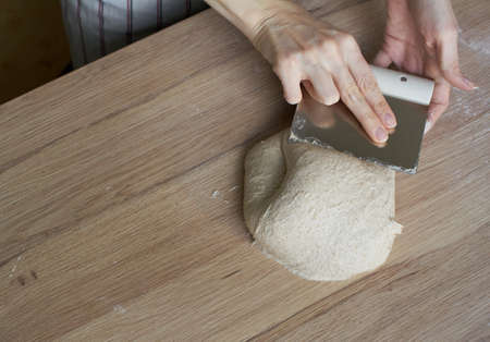 Female hands folding and kneading the dough on a kitchen counter for baking rustic sourdough bread.