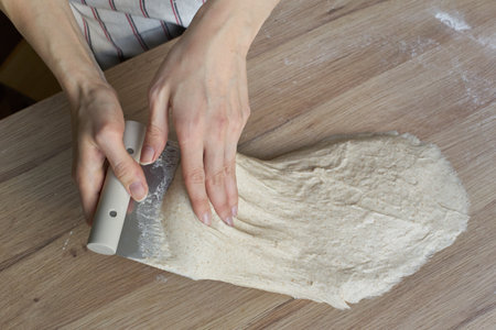 Female hands folding and kneading the dough on a kitchen counter for baking rustic sourdough bread.