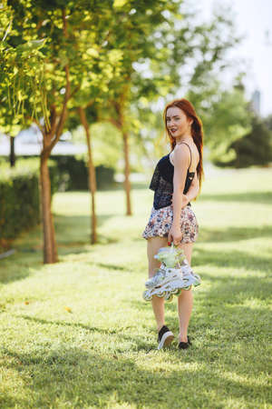 red-haired woman in roller skate in a city park on her T-shirt and bright blue chert in the park grow spruce lined road pavementの写真素材