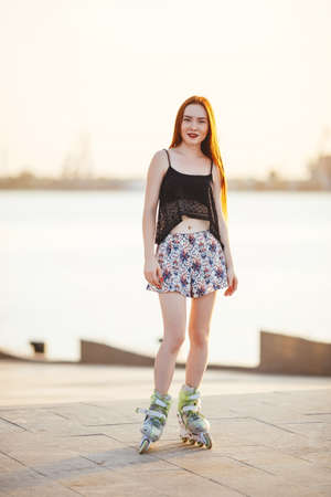 red-haired woman in roller skate in a city park on her T-shirt and bright blue chert in the park grow spruce lined road pavementの写真素材