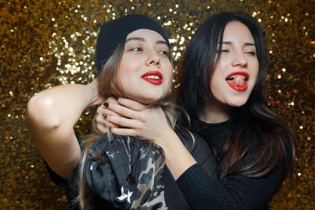 two women dressed black lesbian girlfriends having fun in night clubs photographed on gold background one girl wearing red knit cap and another black scarf with stars them red lipstick and they are very funny and passionate love each otherの写真素材
