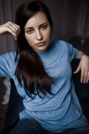 brunette posing in a hotel room sitting in purple chair on her wearing a blue sweater and jeansの写真素材