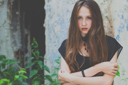 portrait of a beautiful young sad goth girl in an abandoned old building outdoors at the day timeの写真素材