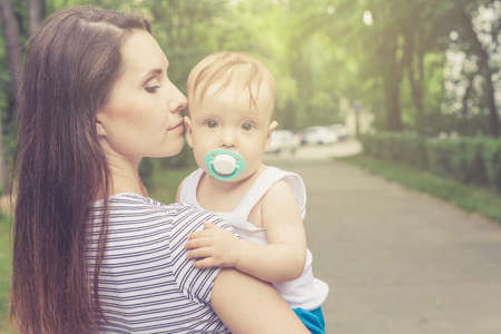 Happy mother playing with her baby in the park on the bench at the day timeの写真素材