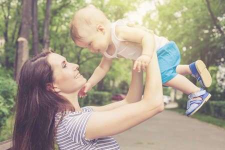 Happy mother playing with her baby in the park on the bench at the day timeの写真素材