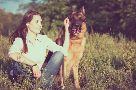 Young beautiful girl with a German shepherd playing on the lawn at the day timeの写真素材