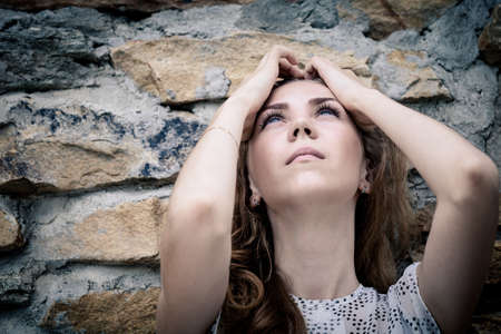 portrait of a beautiful young sad girl standing near the wall outdoors at the day timeの写真素材