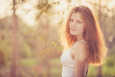 Trendy Hipster Girl Relaxing on the road near tree at the day time. Concept of Modern Youth Lifestyle.  Blowing Long Hair.  Glow Sun, Sunshine. Backlit. Toned in warm colorsの写真素材