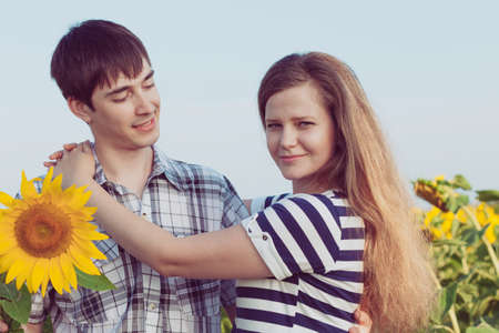 Portrait of young couple standing with sunflowers in a field. Concept of beautiful couple in love.の写真素材