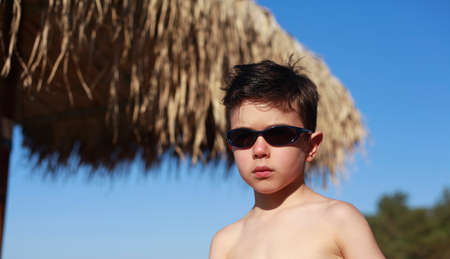 Cute 5 year old Caucasian boy poses on a beach in summer wearing sunglassesの写真素材