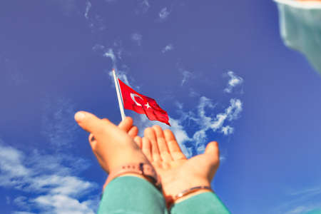 Hands holding a Turkish flag on blue sky background. Turkish national holiday concept.の写真素材