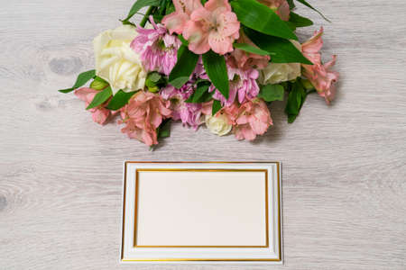 Colorful bouquet of roses, chrysanthemum and alstroemeria flowers with empty photoframe on wooden...
