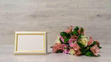 Colorful bouquet of roses, chrysanthemum and alstroemeria flowers with empty photoframe on wooden...