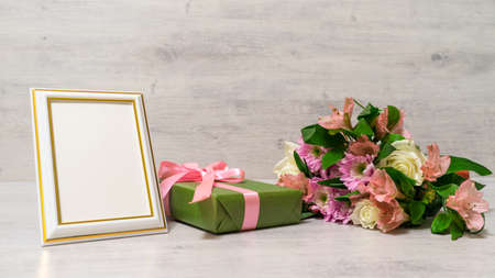 Colorful bouquet of roses, chrysanthemum and alstroemeria flowers with gift box and empty photoframe on wooden backgroundの写真素材