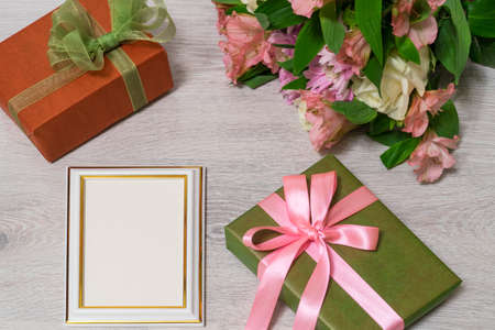 Colorful bouquet of roses, chrysanthemum and alstroemeria flowers with gift boxes and empty photoframe on wooden background