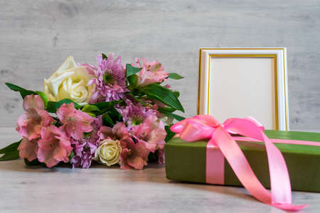 Colorful bouquet of roses, chrysanthemum and alstroemeria flowers with gift box and empty photoframe on wooden backgroundの写真素材