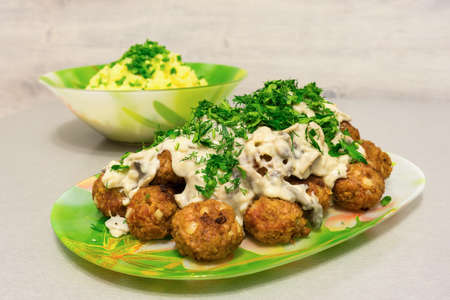 Fried meatballs with stroganoff gravy and mashed potatoes and fresh herbs on a tableの写真素材