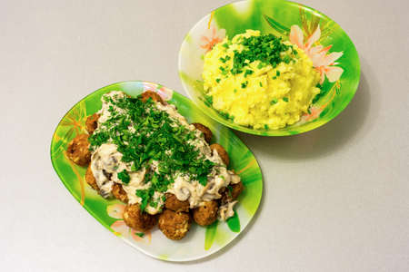 Fried meatballs with stroganoff gravy and mashed potatoes and fresh herbs on a tableの写真素材
