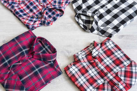 Four multi-colored checkered women's shirts lying neatly folded on a light wooden backgroundの写真素材