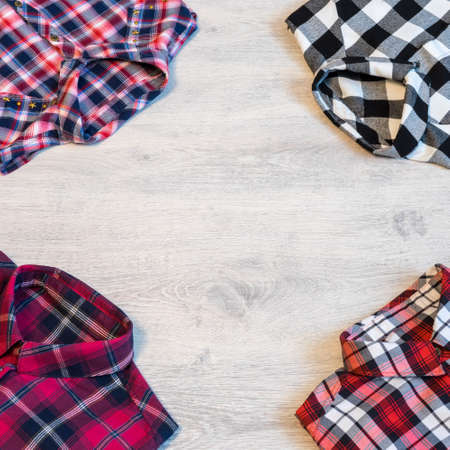 Four multi-colored checkered women's shirts lying neatly folded on a light wooden background