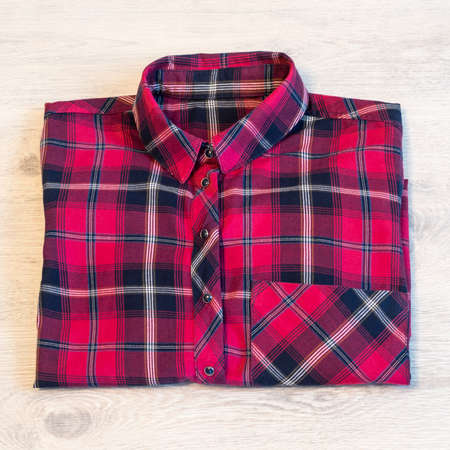 Multi-colored checkered women's shirt lying neatly folded on a light wooden backgroundの写真素材
