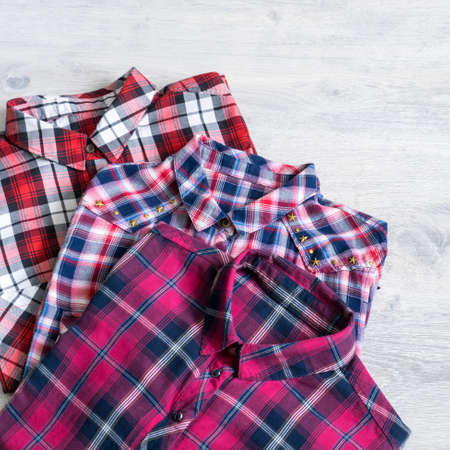 Three multi-colored checkered women's shirts lying neatly folded on a light wooden backgroundの写真素材