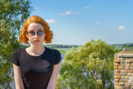 Portrait of young pretty tourist lady in sunglasses sitting on stones of ancient architectural attractions ruins on the blue sky background in sunny summer day. Travel conceptの写真素材