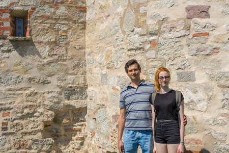 Handsome middle-aged man and young pretty lady in sunglasses standing against ancient architectural...