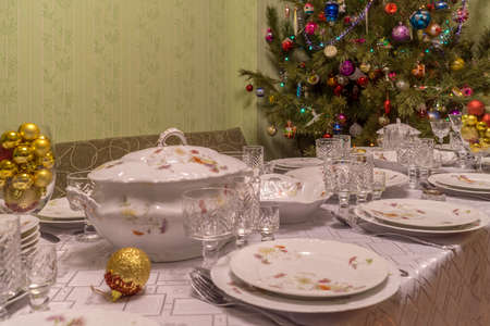 Served table with festive tableware near beautiful decorated Christmas tree in living room interior. Concept of new year holiday at cozy homeの写真素材