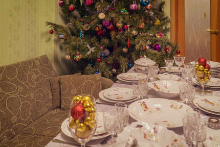 Served table with festive tableware near beautiful decorated Christmas tree in living room interior. Concept of new year holiday at cozy home. Focus on fir, vintage toneの写真素材