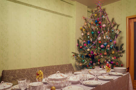 Served table with festive tableware near beautiful decorated Christmas tree in living room interior....