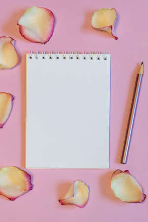 Notebook and pencil with dried cream rose petals on pink pastel paper background. Love or romance concept, mock up. Flat lay, copy space, top viewの写真素材