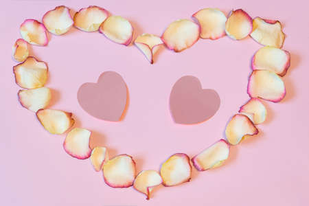 Frame of dried cream rose petals in heart shape with two pink paper hearts on pastel background. Love, romance or Valentine's day concept, mock up. Flat lay, copy space, top viewの写真素材