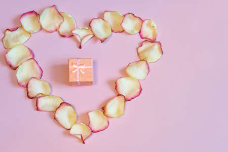 Pink gift box in frame of dried cream rose petals in heart shape on pastel paper background. Love, romance or Valentine's day concept, mock up. Flat lay, copy space, top viewの写真素材