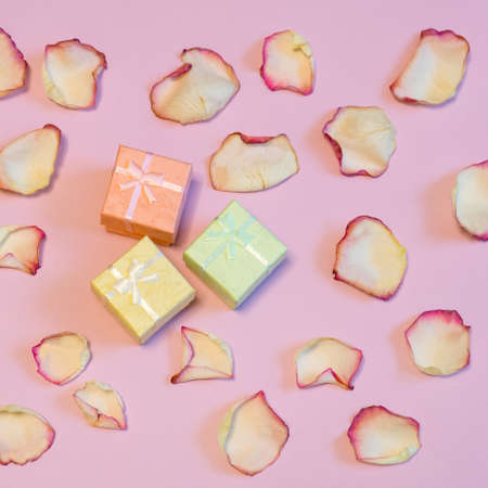 Three gift boxes in pastel colors with dried cream rose petals on pink paper background. Love, romance or Valentine's day concept. Flat lay, copy space, top viewの写真素材