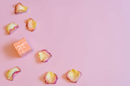 Pink pastel gift box with dried cream rose petals on pink paper background. Love, romance or Valentine's day concept. Flat lay, copy space, top viewの写真素材
