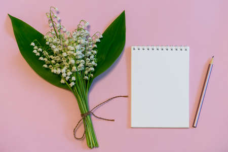 Bouquet of fresh lily of the valley flowers with notebook and pencil on pink pastel background. Beautiful spring layout. Top view, copy space, mock upの写真素材