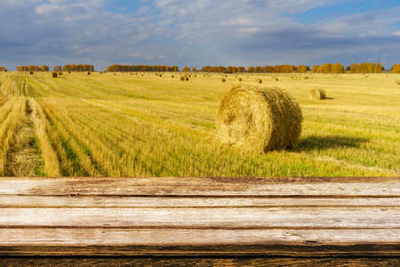 Empty wooden table with blurred autumn landscape of beveled field and straw bales. Can be used for...