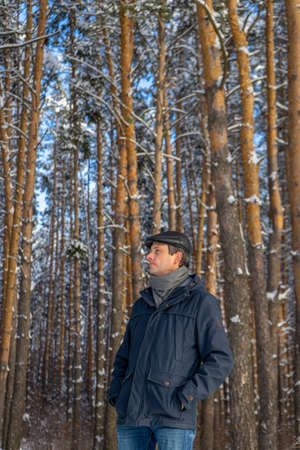 Portrait of handsome middle-aged man against beautiful winter landscape. Man walking in snowy forest in sunny frosty day. Human and nature, winter holidays, weekend at countryside concept.の写真素材