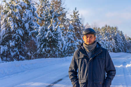 Portrait of handsome middle-aged man against beautiful winter landscape. Man walking along forest road in sunny frosty day. Human and nature, winter holidays, weekend at countryside concept.の写真素材
