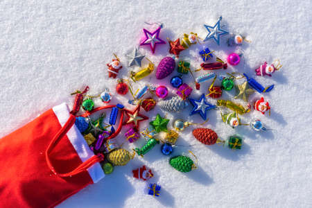 Red bag with many colorful new year toys lying on white fresh snow. Santa Claus scattered bag of gifts. Merry Christmas and Happy New Year. Greeting card for winter holidays. Top view, copy space.の写真素材