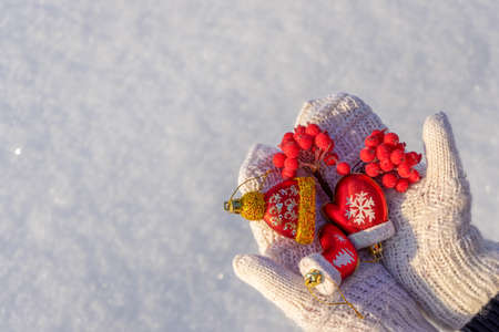 Human hands with open palms in white knitted mittens holding decorative new year toys on fresh snow...