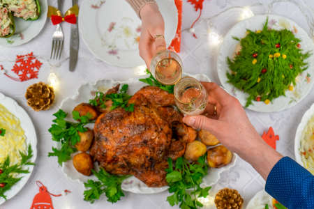Human hands holding glasses with sparkling wine. Friends or family toasting with champagne over festive Christmas table. Xmas dinner, delicious food, winter holidays celebration at cozy home. Top viewの写真素材
