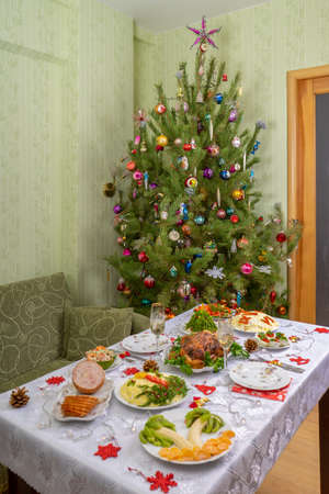 Festive Christmas served table against beautiful green pine tree decorated with many colorful new year toys. Xmas dinner, delicious food, christmas turkey. Winter holidays celebration at cozy home.の写真素材