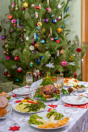 Festive Christmas served table against beautiful green pine tree decorated with many colorful new year toys. Xmas dinner, delicious food, christmas turkey. Winter holidays celebration at cozy home.の写真素材