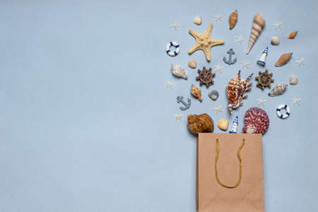 Various decorative nautical items, seashells, sea stars and miniature toys flying from kraft paper bag on blue pastel background. Sea travel, summer vacation at ocean concept. Flat lay, top view.の写真素材