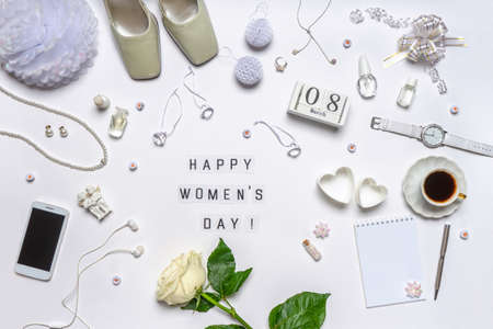 Text HAPPY WOMEN'S DAY. Stylish feminine accessories, decorative items, cosmetics, jewellery, hearts and rose flower on white background. Calendar date 8 March. Flat lay, top view.の写真素材