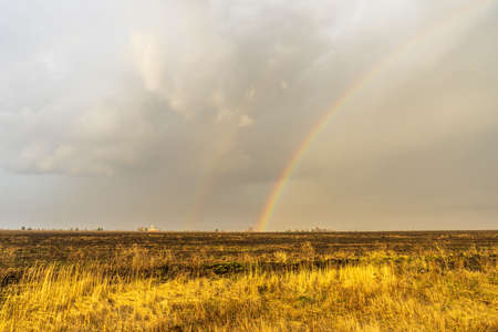 Spring landscape with double rainbow over burned field after thunderstorm. Beautiful natural background.の写真素材