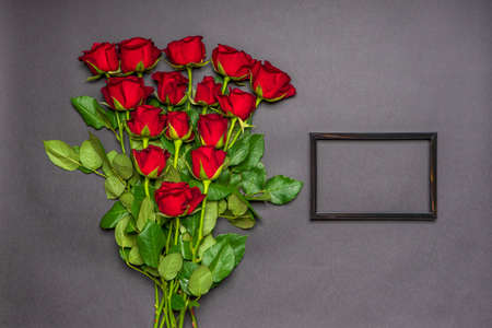Bouquet of fresh red rose flowers and empty photoframe on black background. Floral composition,...
