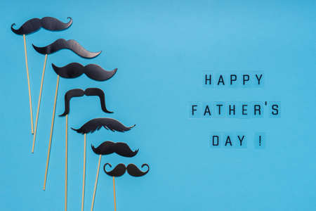 Various black photo booth props moustaches of different shape on blue background. Greeting card, text HAPPY FATHER'S DAY. Flat lay, top view.の写真素材
